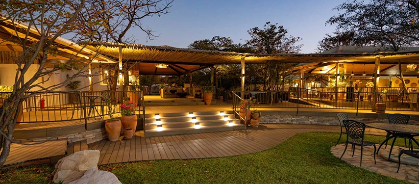 The open deck and lantern-lit lounge at Insika Lodge create a warm and elegant space overlooking the surrounding wilderness at dusk.