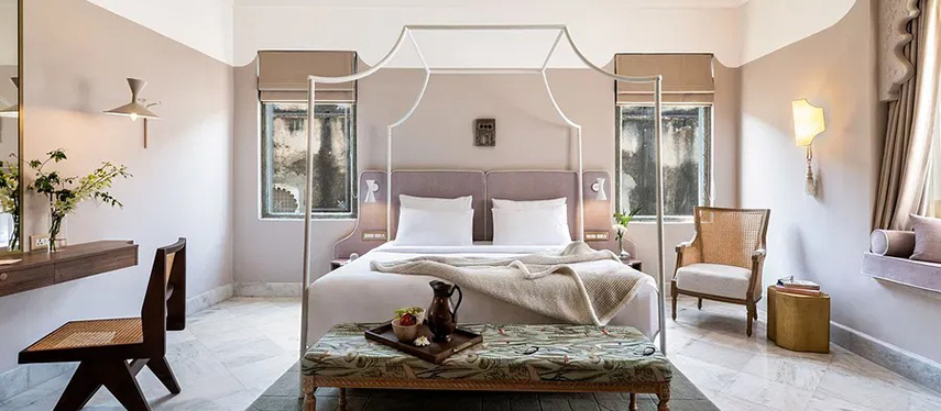 Softly lit guestroom featuring a four-poster bed, natural textures, and traditional Rajasthani window framing – Jhilwara Haveli