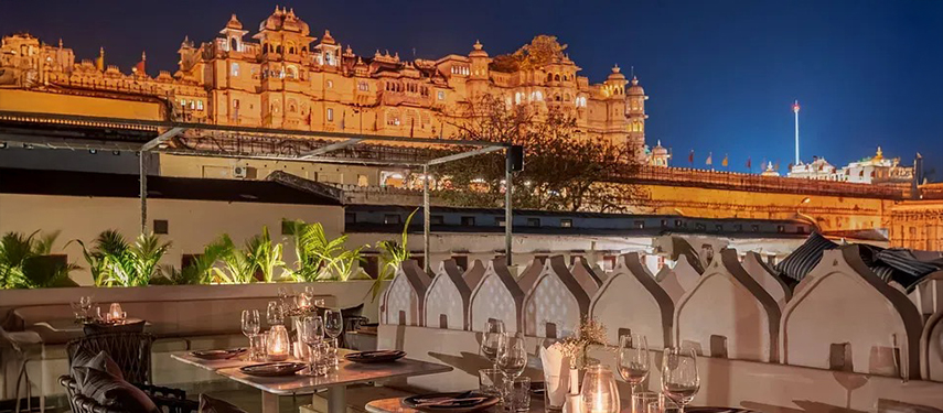 Romantic rooftop dinner setting overlooking the illuminated City Palace at night