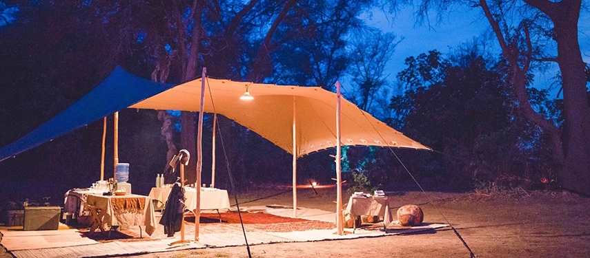 Open-sided dining tent set beneath canvas and lantern light at Kutali Camp in the evening.