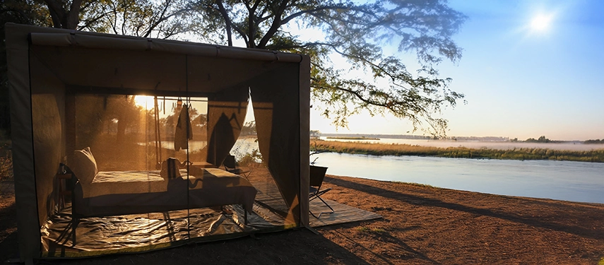 Canvas safari tent positioned on the riverbank overlooking the Zambezi at sunrise.