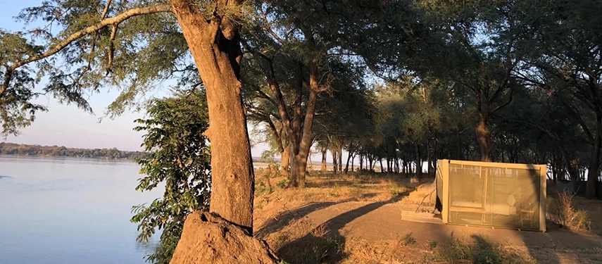 Safari tent pitched on the riverbank at Kutali Camp with golden evening light filtering through the trees.