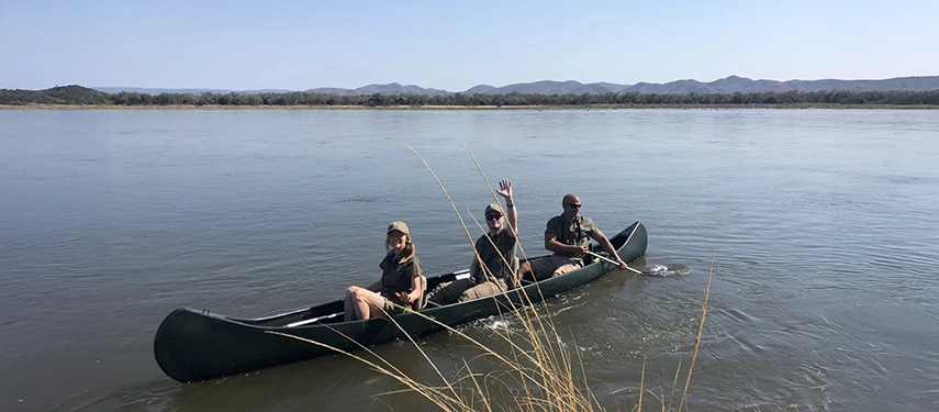 Guests paddling a canoe across the wide Zambezi River under a clear blue sky.