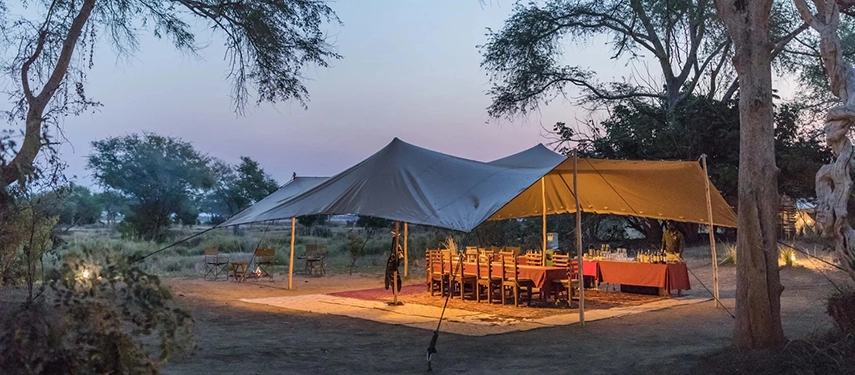 Evening dining tent illuminated by lanterns, with a long table set for dinner in the bush.