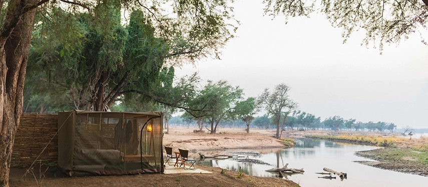 Safari tent with open sides overlooking a peaceful river channel at Kutali Camp.