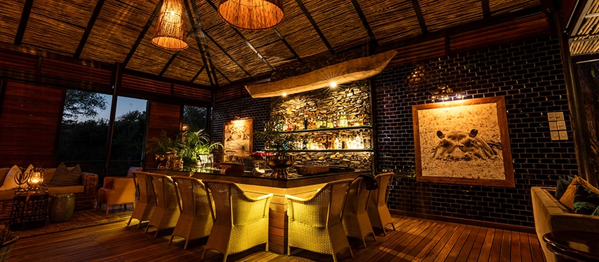 The main guest area at Mukwa River Lodge features an open-air bar and lounge, softly lit to create an atmospheric space for evening relaxation.