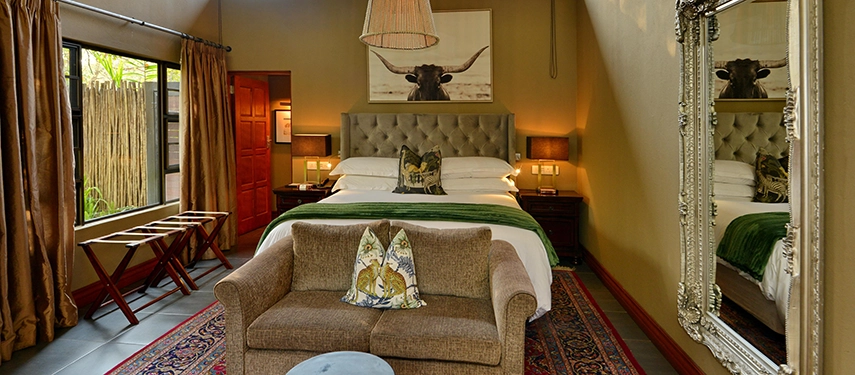 A beautifully styled bedroom at Mukwa River Lodge features soft textiles, African-inspired artwork, and doors opening onto a private outdoor space.