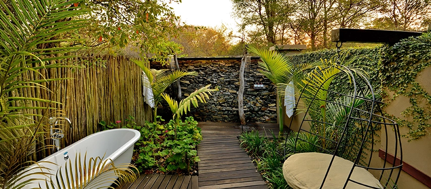 An outdoor bath at Mukwa River Lodge is set within a private garden courtyard, framed by natural stone walls and lush greenery for secluded relaxation.