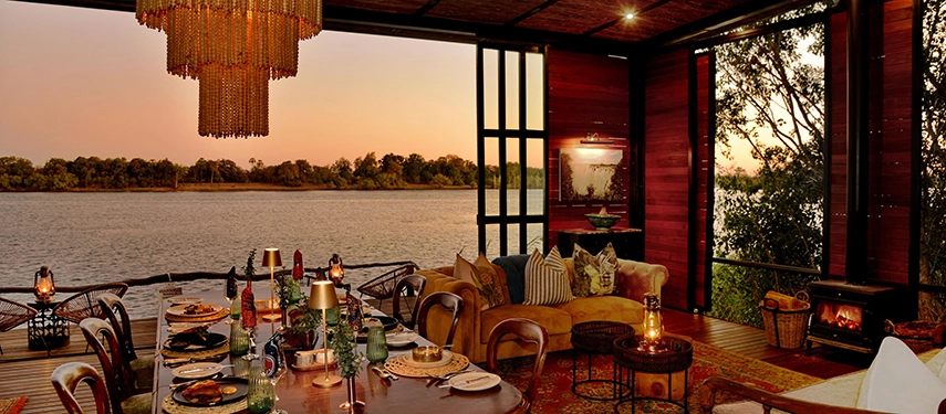 The open river lounge at Mukwa River Lodge is styled with warm lighting and comfortable seating, overlooking the Zambezi River at sunset.