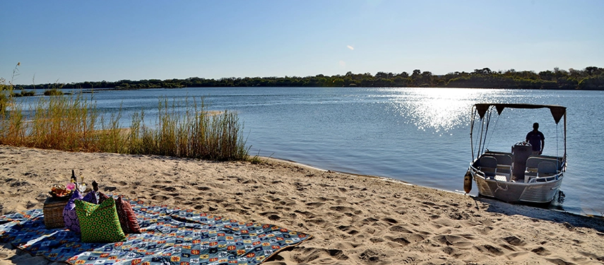A secluded riverside picnic is arranged on a sandy bank of the Zambezi River, reached by boat from Mukwa River Lodge.