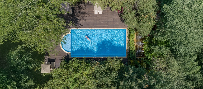 An aerial view reveals the swimming pool at Mukwa River Lodge, surrounded by dense greenery and offering a peaceful retreat from the heat of the day.