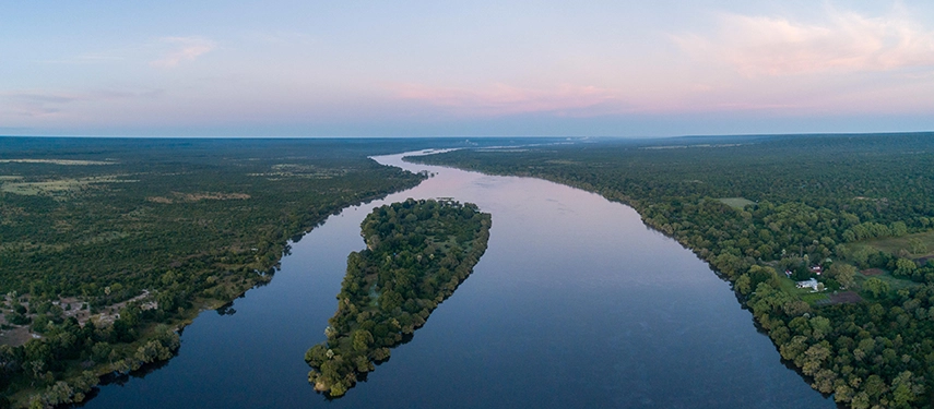 The Zambezi River winds through a vast green landscape in this aerial view, illustrating the serene riverside setting of Mukwa River Lodge near Victoria Falls.