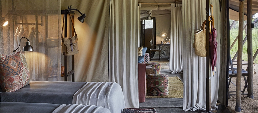 Twin beds inside a tented suite at Nyasi Tented Camp open toward a comfortable lounge area, styled with natural textures and soft safari tones.