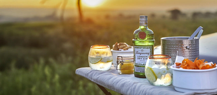 A classic bush gin and tonic is served at sunset, overlooking the Serengeti plains near Nyasi Tented Camp as golden light fades into dusk.