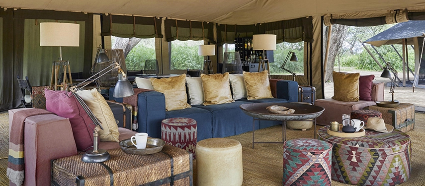 The main lounge at Nyasi Tented Camp features deep sofas, textured cushions, and relaxed safari styling beneath canvas overlooking the Serengeti.