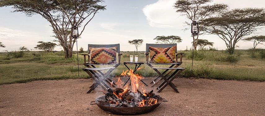 Sundowner drinks are enjoyed beside a crackling campfire at Nyasi Tented Camp, with safari chairs set against the open plains.