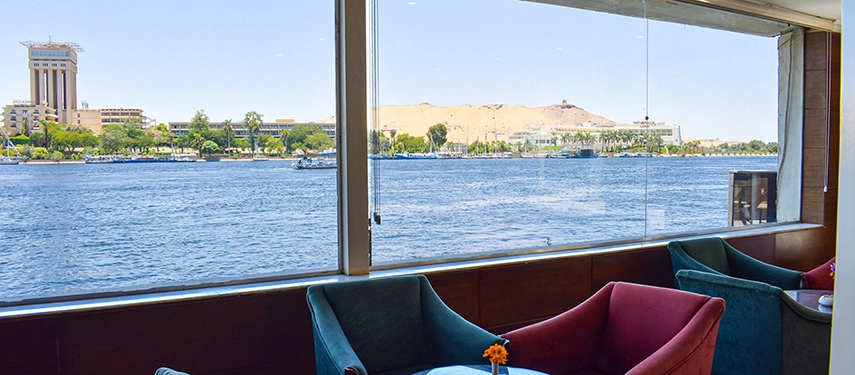 A sweeping view over the pool terrace and the Nile at sunset with feluccas drifting past and golden light on the hills.