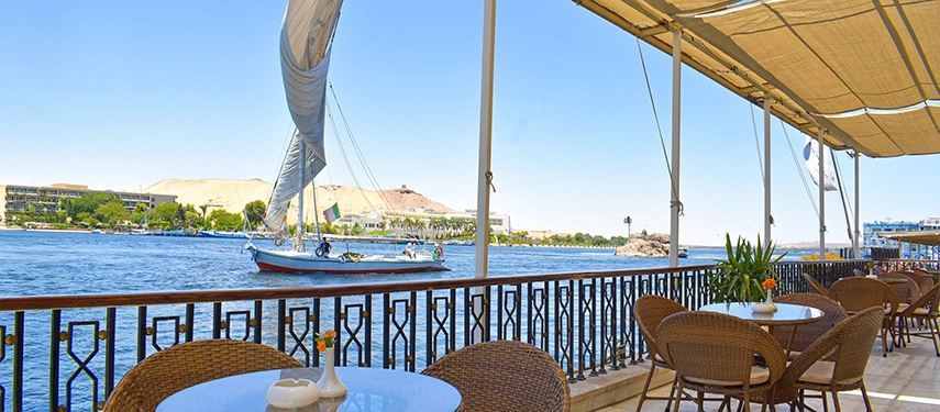 A shaded terrace café overlooking the Nile with wicker chairs and feluccas sailing past in the midday breeze.