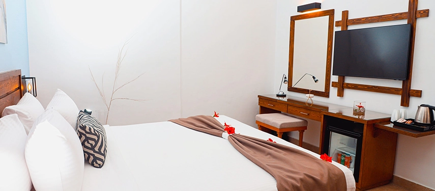 A fresh, minimalist guest room with a neatly made bed, wooden furniture and soft lighting ideal for a restful night.