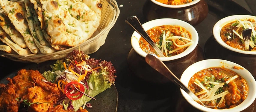 A vibrant vegetarian Indian meal with bowls of curry, naan bread, pakoras, and a fresh salad garnish.
