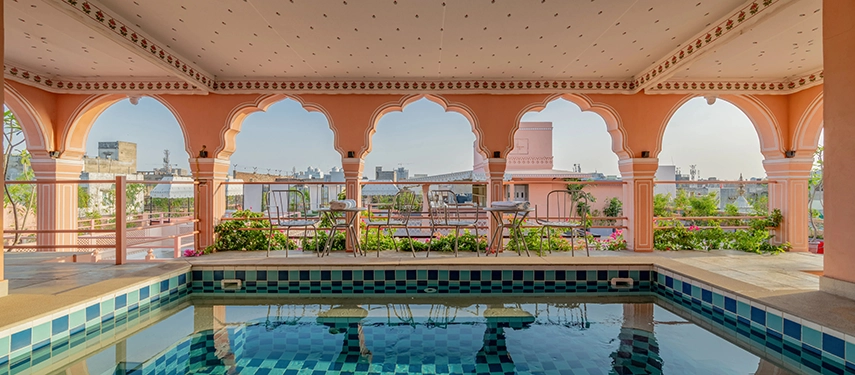 A rooftop plunge pool framed by pink arches, with a view over Jaipur’s cityscape.