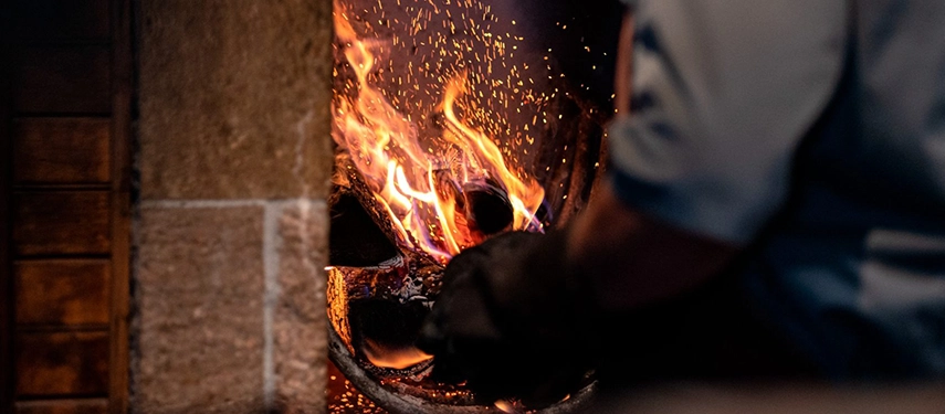 Sparks rise from an open fire as a chef tends glowing embers, preparing traditional Patagonian cuisine.