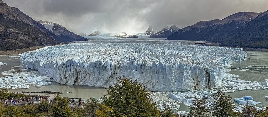 The immense face of Perito Moreno Glacier towers above the lake as visitors stand in awe on viewing platforms below.
