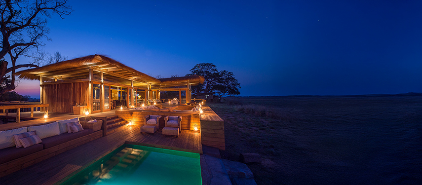 Shumba Camp’s main lounge and pool warmly lit at sundown