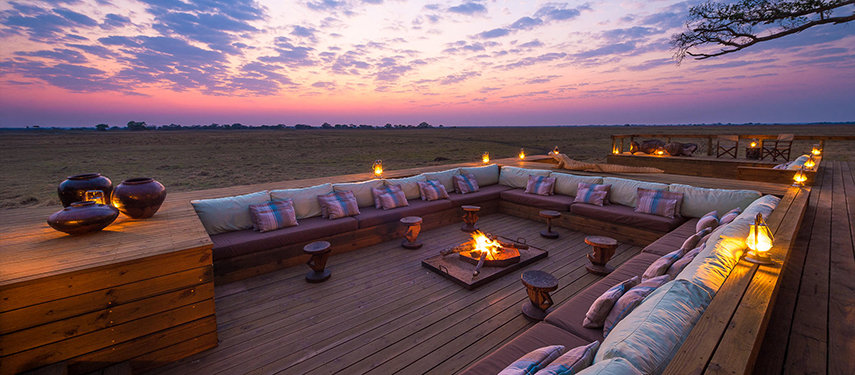 Sunset view from Shumba Camp’s deck lounge with a blazing central fire and plush seating