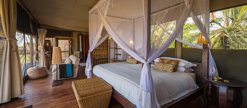 Safari tent interior featuring a canopied king bed and views into the surrounding wilderness