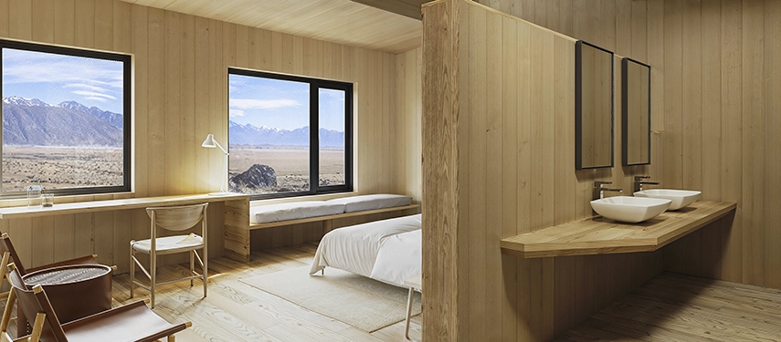 A serene timber-clad room frames sweeping steppe and mountain views through wide windows, offering calm Patagonian simplicity.