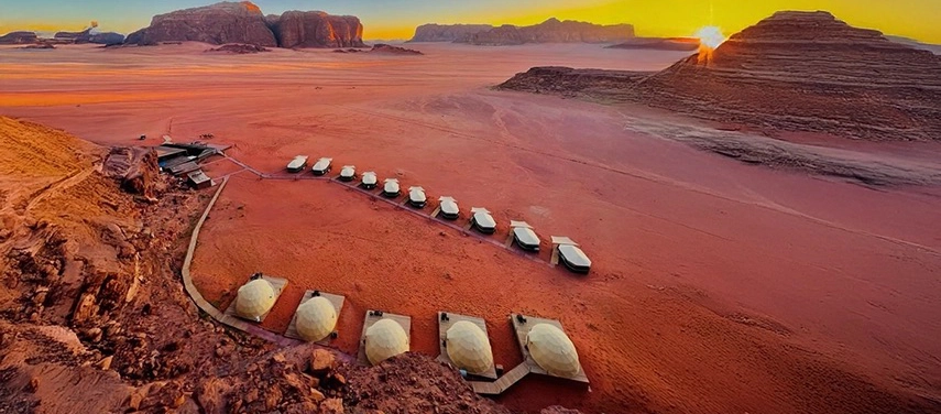 The camp curves gently across the desert floor at sunrise, with soft light illuminating the domed tents and vast open plains.