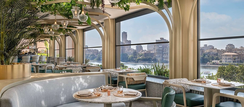 A chic riverside restaurant framed by arched windows offers elegant dining with views across the Nile and Cairo’s leafy banks.