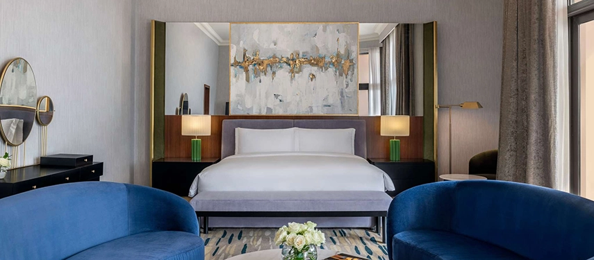 A contemporary Sofitel Cairo Nile Hotel suite features deep blue seating, soft lighting, and a central king bed framed by modern artwork.