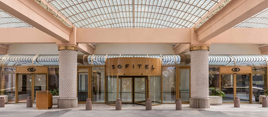 The Sofitel Cairo Nile Hotel entrance features a gold revolving door beneath a glass canopy supported by textured columns.