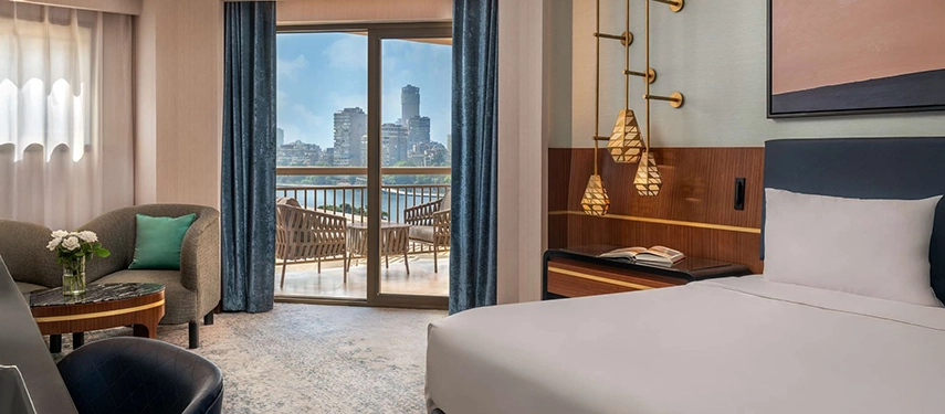 A stylish guest room with soft blue accents opens onto a private balcony overlooking the Nile and Cairo’s skyline.