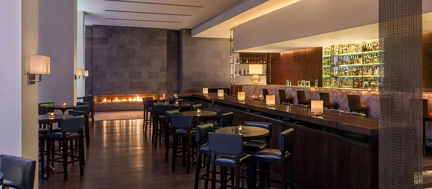 The hotel’s chic bar features dark timber, soft lighting, and a glowing linear fireplace that adds an intimate atmosphere.