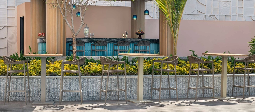 An outdoor pool bar lined with high stools sits among tropical greenery and soft pastel tones.