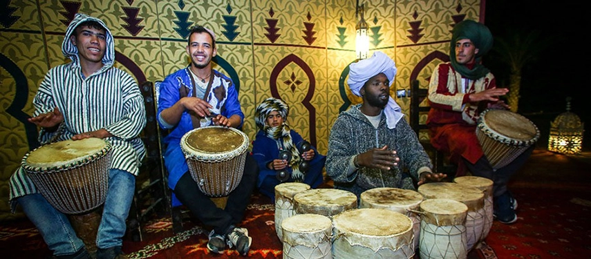 Group of musicians in traditional dress performing with hand drums inside the Berber tent.