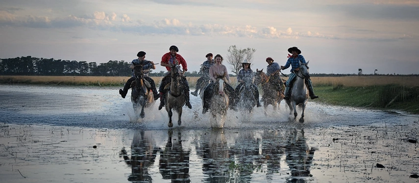 Group of gauchos and riders galloping through shallow wetland waters at Estancia Don Joaquín.