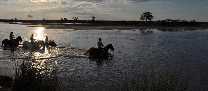 Riders on horseback crossing a reflective river at sunset at Estancia Don Joaquín.