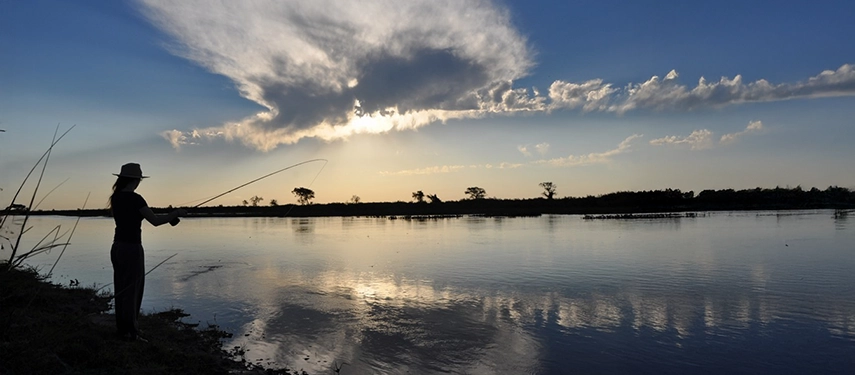 Person casting a fishing line across a tranquil river at sunrise at Estancia Don Joaquín.