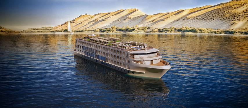 A&K Sanctuary Nile Seray cruising the Nile beneath sweeping sand dunes, its elegant profile reflected in the still river.