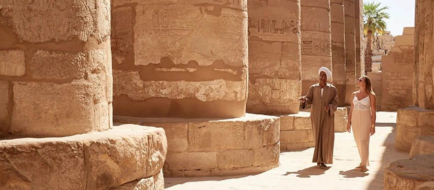 Guests exploring an ancient Egyptian temple with a private Egyptologist guide, walking between towering stone columns carved with hieroglyphs.