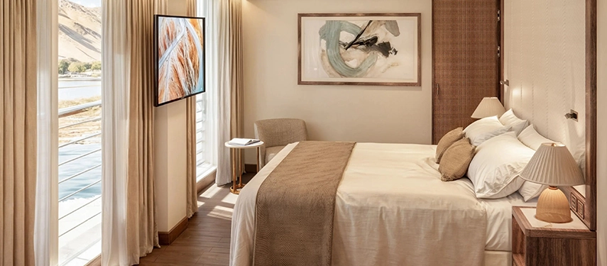 A refined river-facing suite aboard A&K Sanctuary Nile Seray with warm neutral tones, floor-to-ceiling windows and serene Nile views.