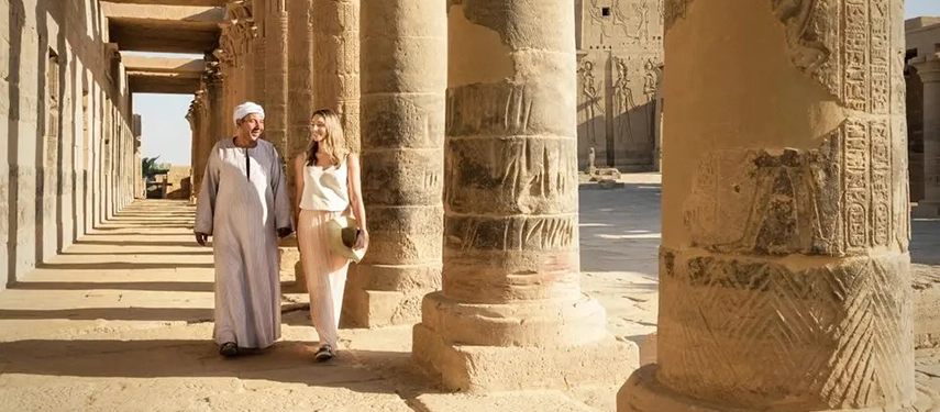 Guests strolling through an ancient Egyptian temple colonnade with a private guide, surrounded by towering carved stone pillars.