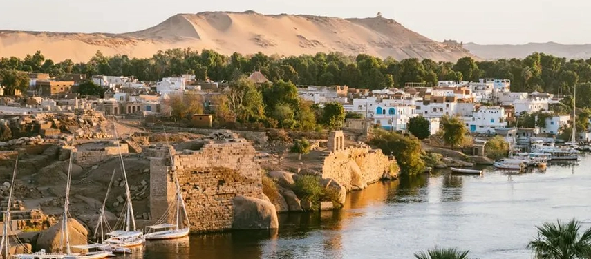 Riverside villages and historic ruins lining the Nile, with whitewashed buildings, palm trees and desert hills rising behind.