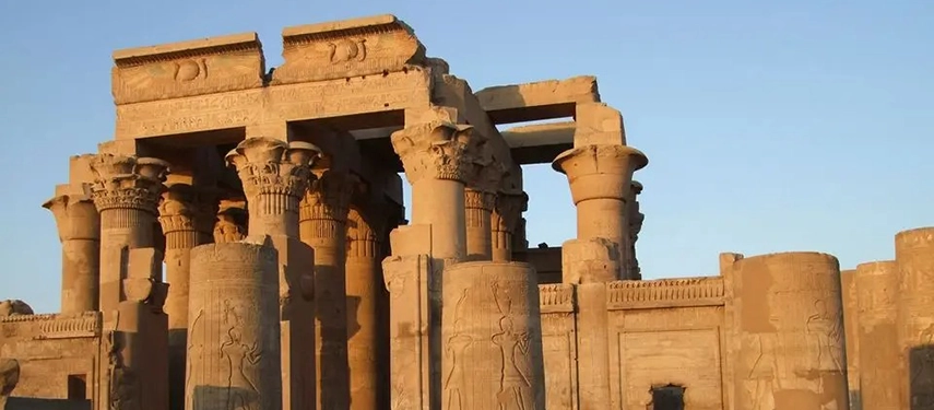 The monumental columns of an ancient Egyptian temple glowing in warm late-afternoon light beneath a clear sky.