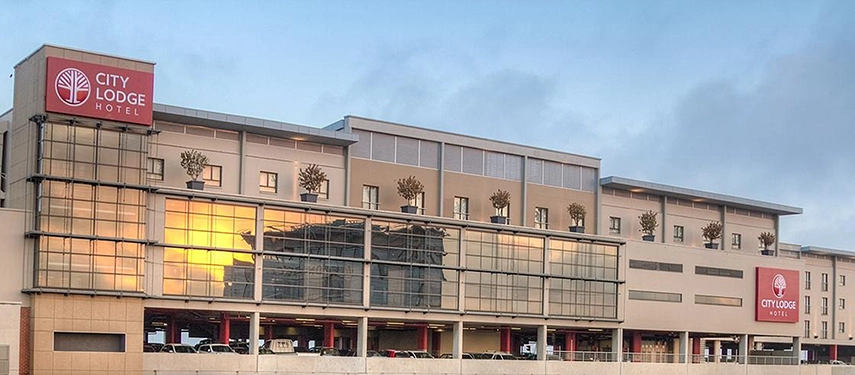 A daytime view of the modern hotel facade, standing conveniently above a parking structure and surrounded by touches of vibrant greenery.