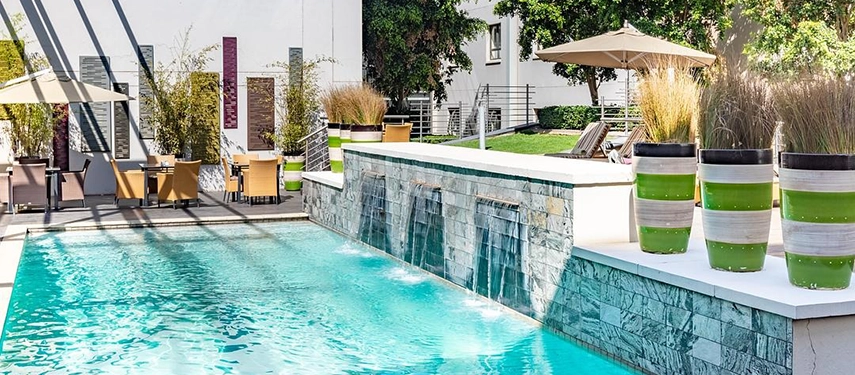 A sparkling outdoor pool area surrounded by wooden decking, comfortable lounge seating, and distinctive striped planters holding ornamental grasses.